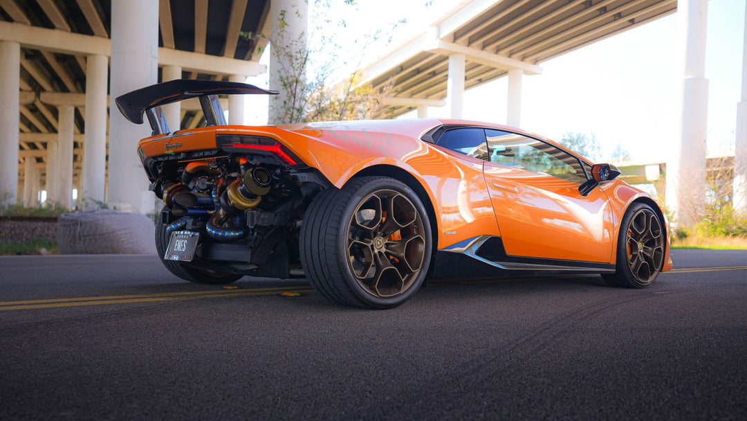 Orange Lamborghini Huracán Performante with a Project Gamma twin-turbo kit, photographed from the rear three-quarter with both turbochargers and the exhaust exiting straight through the rear bumper.