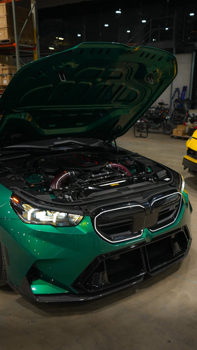 Green BMW M5 G90 with the hood open, showing Project Gamma carbon fiber intakes