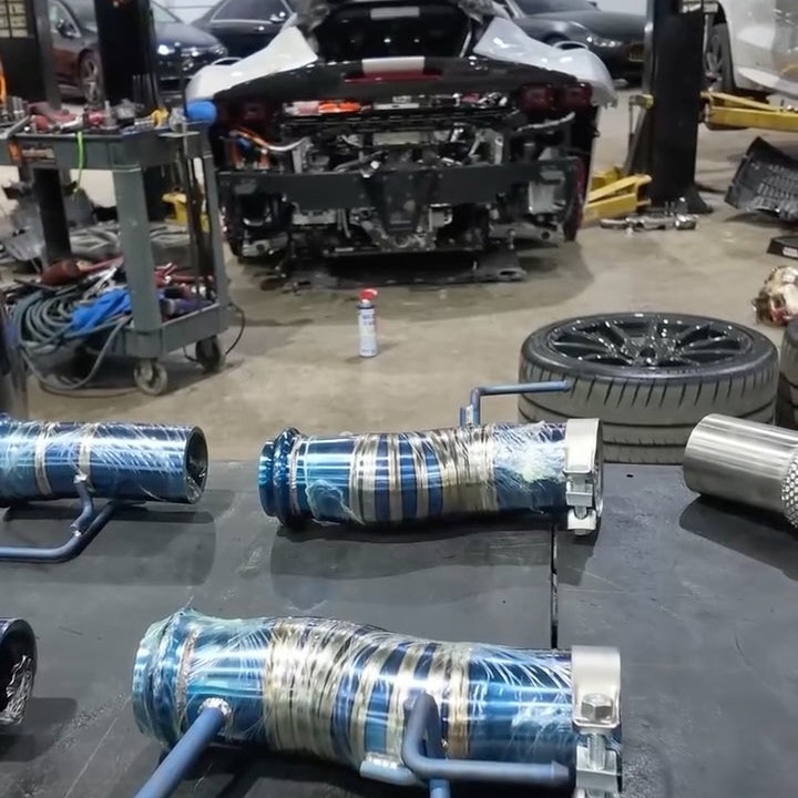 Instagram reel: Titanium race exhaust sections on a bench with a Ferrari SF90 on the lift behind