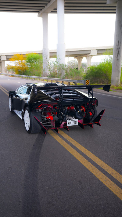 Black Lamborghini Huracán with a carbon rear wing and Project Gamma twin turbo kit, parked under a highway overpass