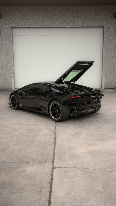 Black Lamborghini Huracán with its engine cover raised in front of a workshop door